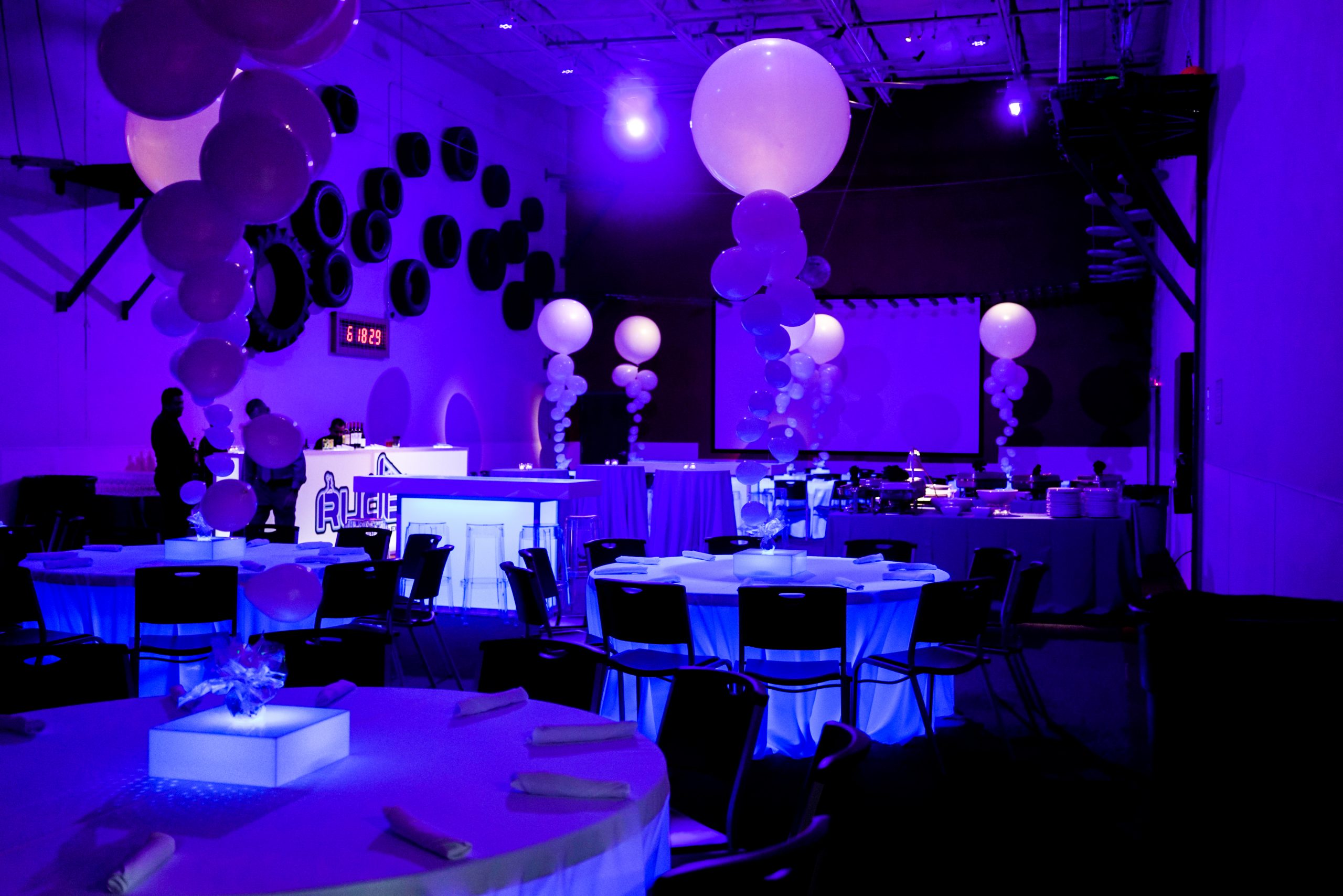 Event room set up with black lights, balloons, tables and chairs, during a private event at Group Dynamix