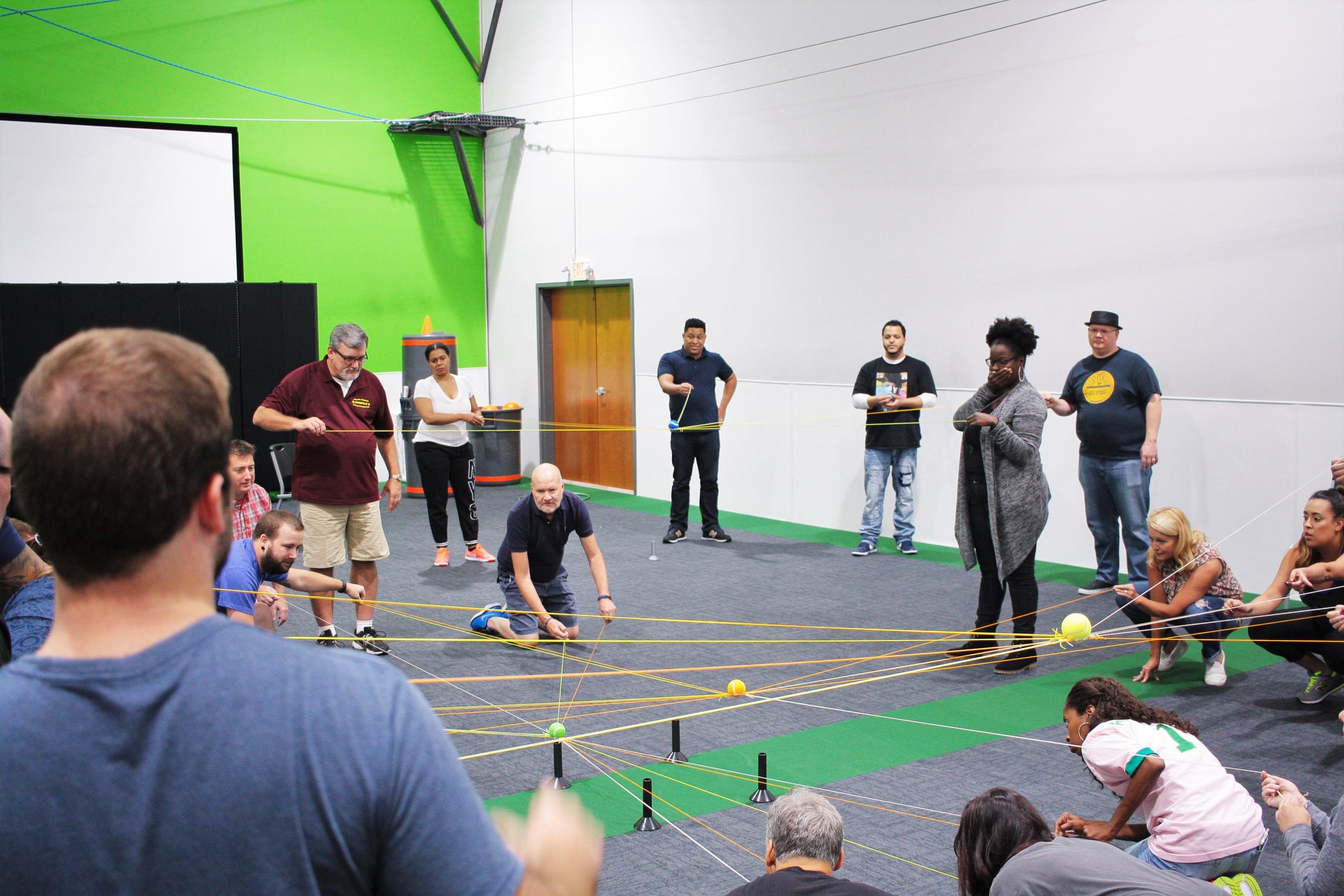 Large group of adults doing a focused team building activity with strings and a ball at Group Dynamix