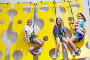 Three teenage girls smiling on a high ropes course at Group Dynamix