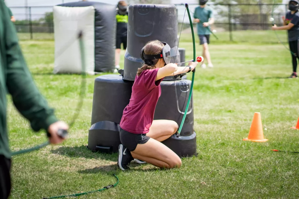 Teenage girl shooting an arrow during an archery tag game at a portable event