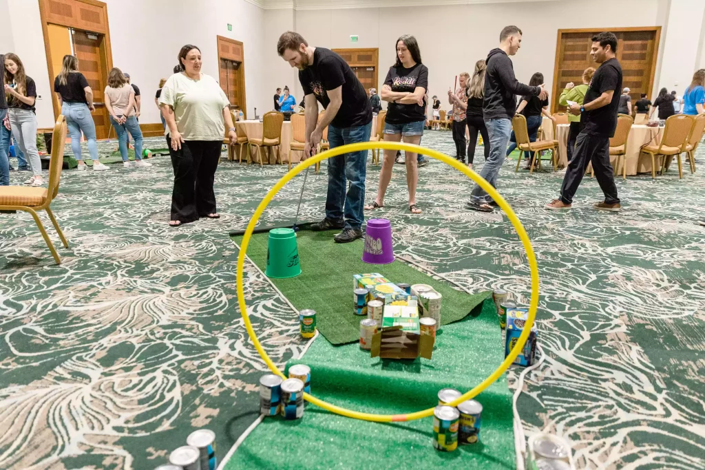 Corporate team playing mini golf on a course built with donated cans of food during a charity event 