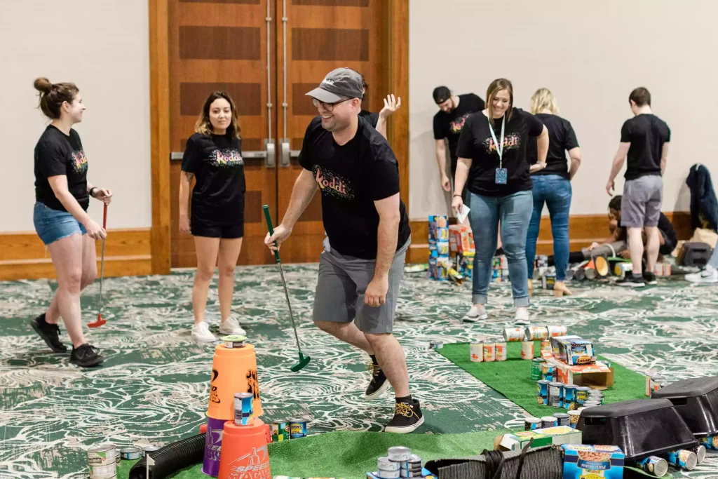 Team of colleagues laughing while playing mini golf during a charity event 