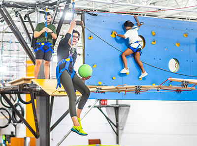 Lady zip lining while holding a dodge ball at Group Dynamix