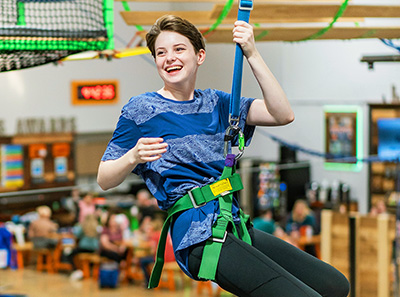 teenage girl zip lining and smiling on the ropes course at Group Dynamix