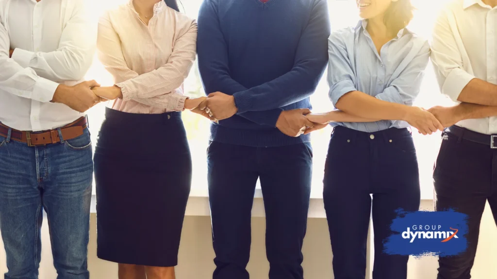 Coworkers standing in a row, linking arms to demonstrate unity and team bonding, with the Group Dynamix logo in the corner.