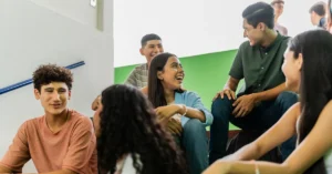 High school students sitting on stairs, laughing and connecting through student leadership games and team building activities designed to build communication and collaboration skills.