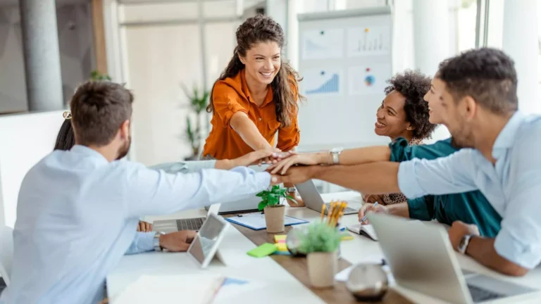 Team members stacking hands together during a meeting to build trust in teams through collaboration and shared commitment.